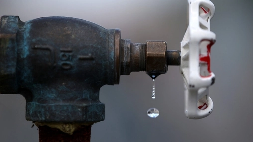 Close-up of an aged brass water valve with a white plastic handle, water droplets dripping from the fitting