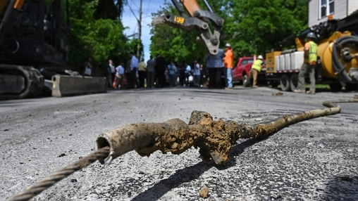 Rusted lead service pipe removed from the ground lying on a road at an active utility excavation site