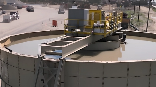 Circular wastewater clarifier with a yellow mechanical bridge and processing unit at an active industrial site