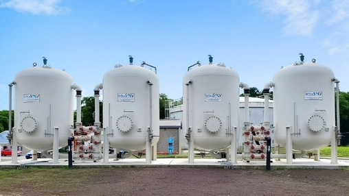 Four large white filtration tanks bearing TetraSolv branding on a concrete base at an outdoor treatment site
