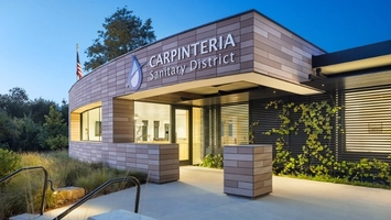 Carpinteria Sanitary District building entrance with modern cladding, warm lighting, and an American flag