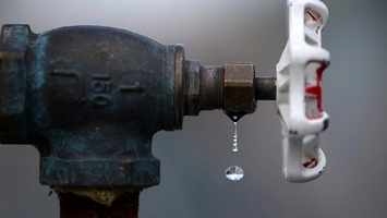 Close-up of an aged brass water valve with a white plastic handle, water droplets dripping from the fitting
