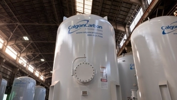White cylindrical industrial tank with a bolted manway and branded label inside a metal-roofed warehouse